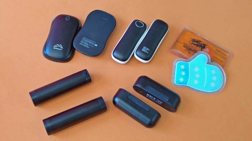 Vier elektronische Hand- und Taschenwärmer neben zwei klassischen Wärme-Pads.