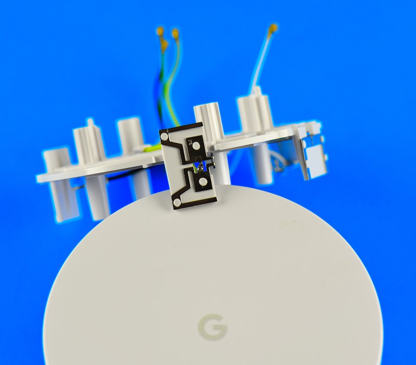 Herausgeholt: Ganz oben in der Google Wifi Mesh Dose sitzt ein Plastik-Kranz mit vier Blech-Antennen. Diese sind über vier Antennen-Kabel mit der grünen Hauptplatine im Boden des Google Access Points verbunden. Die Antennen dienen erstens für die drahtlose Selbst-Vernetzung der Mesh Points untereinander. Zweitens geben sie das Internet drahtlos an die WLAN-End-User weiter (Bild: Harald Karcher).