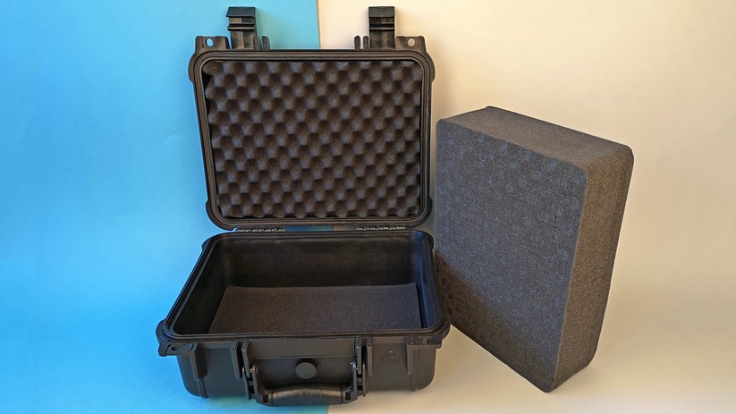 Der Koffer mit Schaumstoffeinlagen in Boden und Deckel. Daneben liegt das Inlay, der  Würfelschaumstoff.