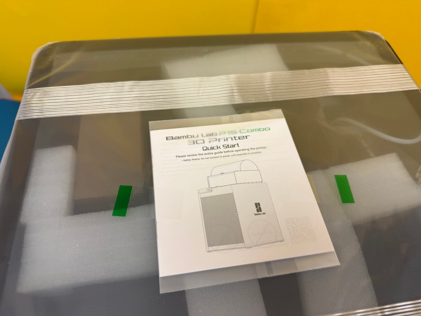 Oben auf dem Drucker, unter der Folie, befindet sich die gedruckte Aufbauanleitung in englischer Sprache. 