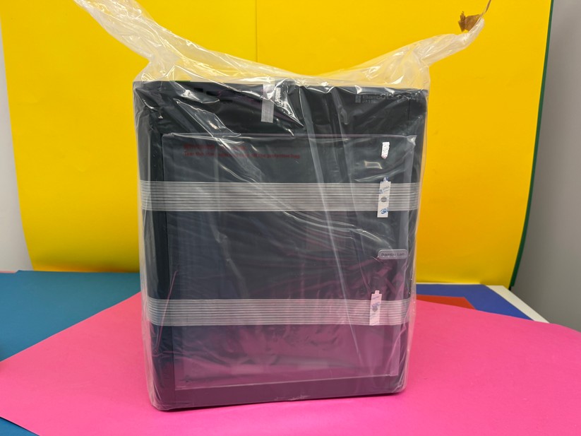 Man hebt den Drucker an der Plastiktüte aus dem Karton. Dabei ist eine zweite Person hilfreich. 