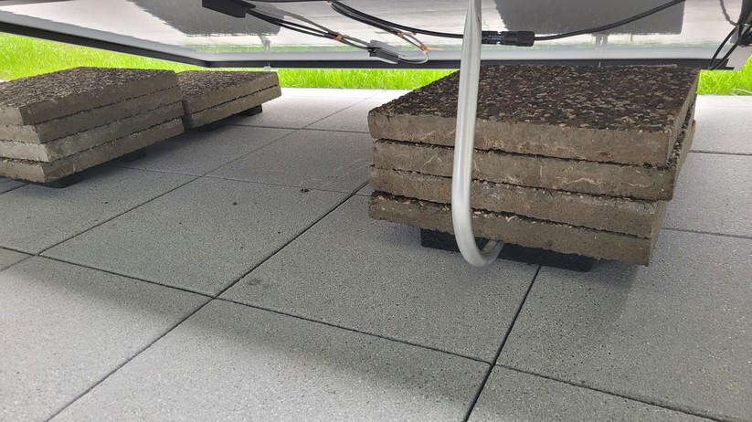 Balkonstrom Premium Flat 800: Die Halterung muss mit Betonplatten beschwert werden. Die MC-4-Kabel befestigen wir mit den am Modul befindlichen Klebestreifen sowie wie mit den mitgelieferten Kabelklemmen, die Halt am Modulrand finden.