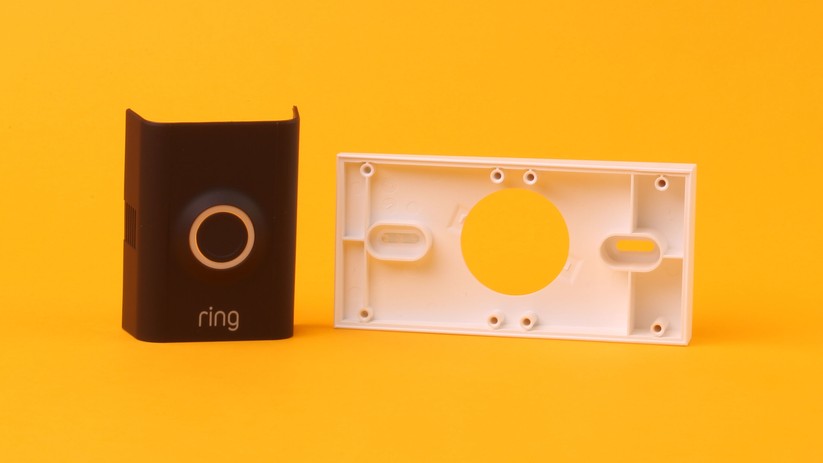 Diverse mitglieferte Anbauteile helfen dabei, Ring passend einzurichten. Links ist die alternative, schwarze Frontblende zu sehen, rechts ein Montageadapter, der die gesamte Einheit nach oben oder unten ausrichtet.