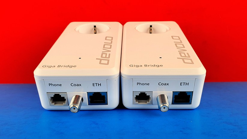 Devolo Giga Bridge: Die beiden Koax-Bridge-Adapter sind auch unten voll identisch. Mittig sieht man einen langen Koax-Stutzen für den Anschluss an eine TV-Koax-Dose. Rechts außen sitzt ein Ethernet-LAN-Adapter für den Anschluss eines Routers oder Rechners.Links außen sieht man einen Phone-Adapter. Damit könnte man so eine Daten-Brücke auch über eine freie Telefon-Kupfer-Leitung bauen, alternativ zur Koax-Brücke. 
