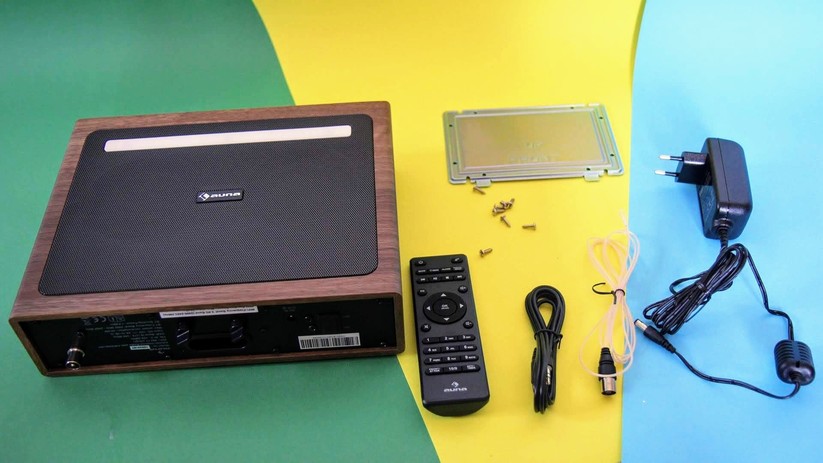 Zum Lieferumfang gehört zusätzlich zum Gerät, Betriebsanleitung und Stromkabel, die Fernbedienung inklusive zweier AAA-Batterien, eine Wurfantenne mit Koaxialanschluss sowie ein Audiokabel mit 3,5mm-Stecker an beiden Enden. Der Montagesatz für das Anbauen an Regalbretter oder Hängeschränke umfasst eine Schiene und acht Schrauben.