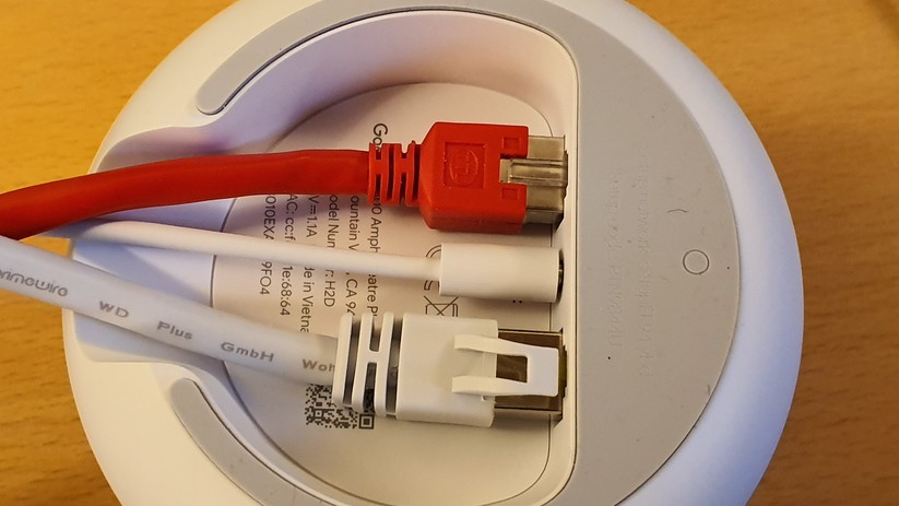 Am roten LAN-Kabel werden im Test 500 Megabit Internet von Vodafone über eine AVM Fritzbox 6591 Cable in den weißen Google Nest Wifi Router zugespielt. Unten: Am weißen Kabel werden hausinterne Daten, Fotos und Videos aus einem 10-Gigabit-Synology DS1618+ NAS-Server zugeliefert. Mitte: Stromkabel vom Netzteil her kommend (Bild: Harald Karcher).