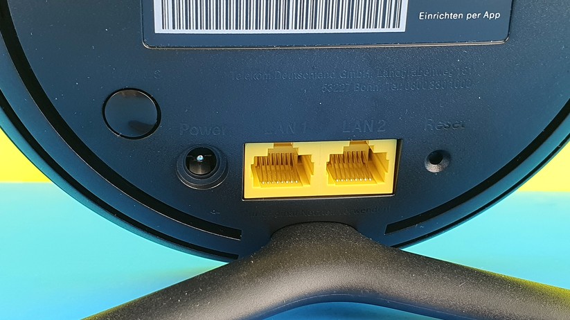 Die schwarz-auf-schwarz-gestanzte Beschriftung der weiteren Elemente ist extrem schlecht lesbar: Links ein echter Ein-Aus-Schalter, daneben Power-In. Mittig zwei gelbe Gigabit-LAN-Buchsen. Rechts ein Reset-Taster-Loch, etwa für eine aufgebogene Büroklammer.