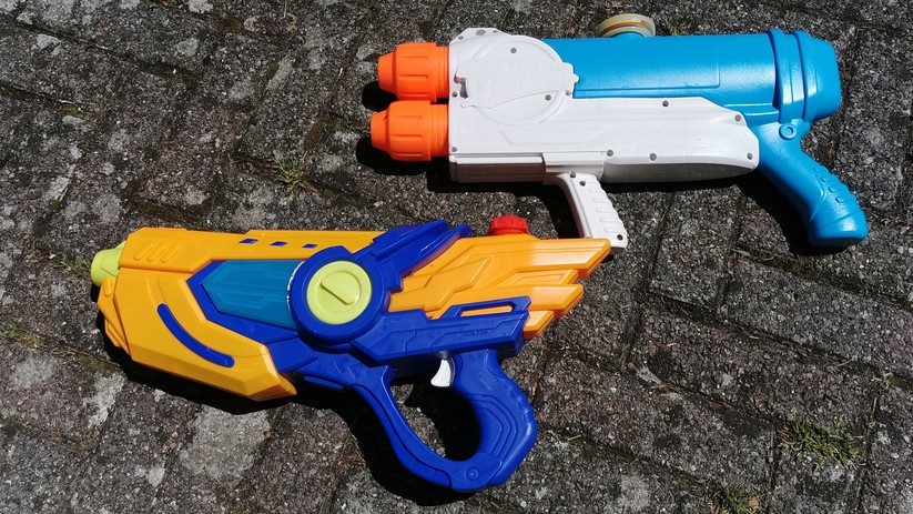Eine günstige elektrische Wasserpistole neben einem Supersoaker mit manuellem Pumpsystem.